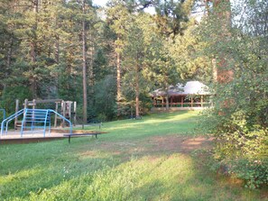 Un parque con un área de juegos, mesas para picnic y un pabellón cubierto rodeado de árboles.