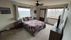Ein Schlafzimmer mit Bett, Deckenventilator, Fernseher und Fenstern mit Vorhängen.