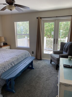 A bedroom with a bed, a bench, a chair, a desk, a ceiling fan, and a window with curtains.