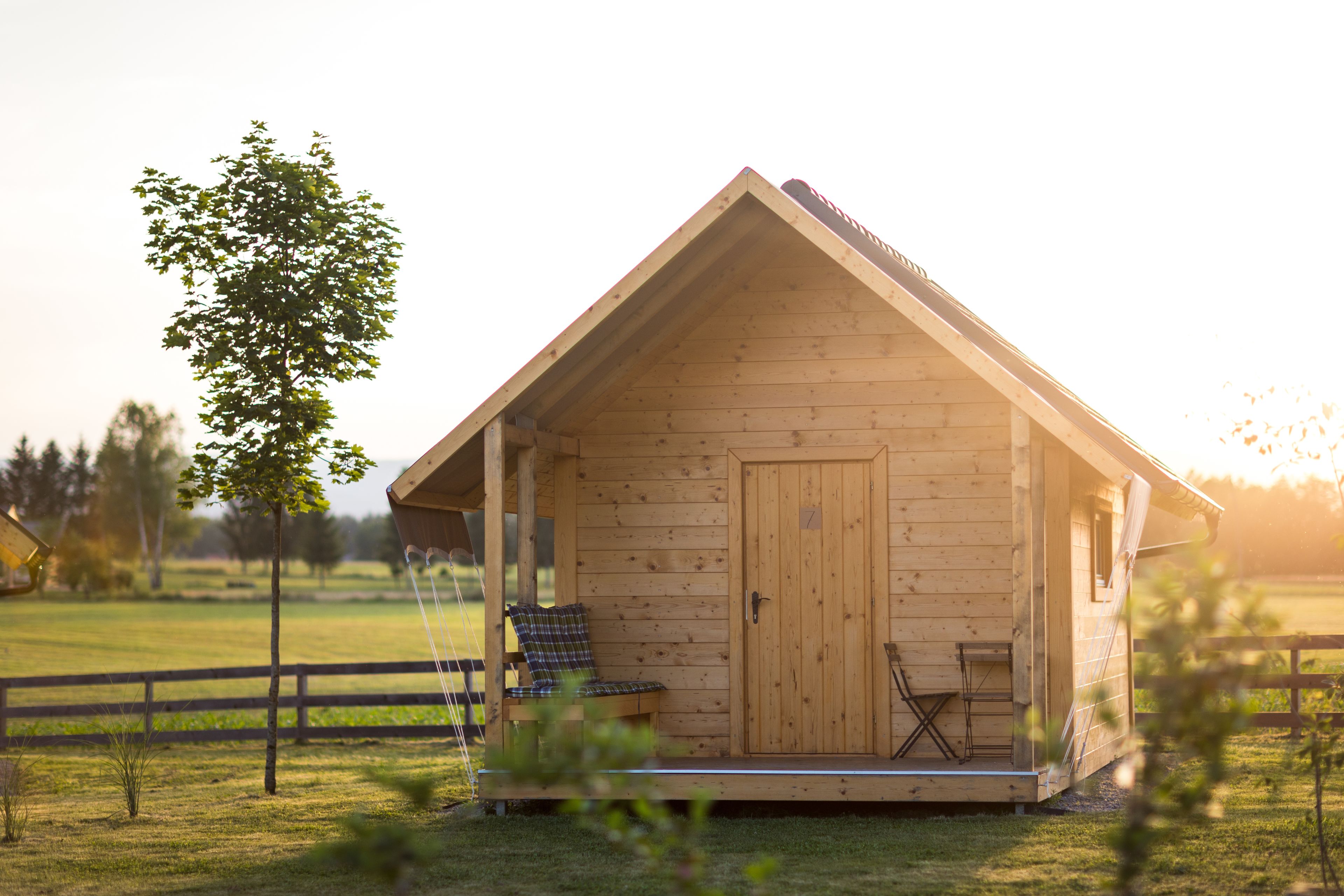 A wooden cabin with a porch, a door, and a small table and chair set.