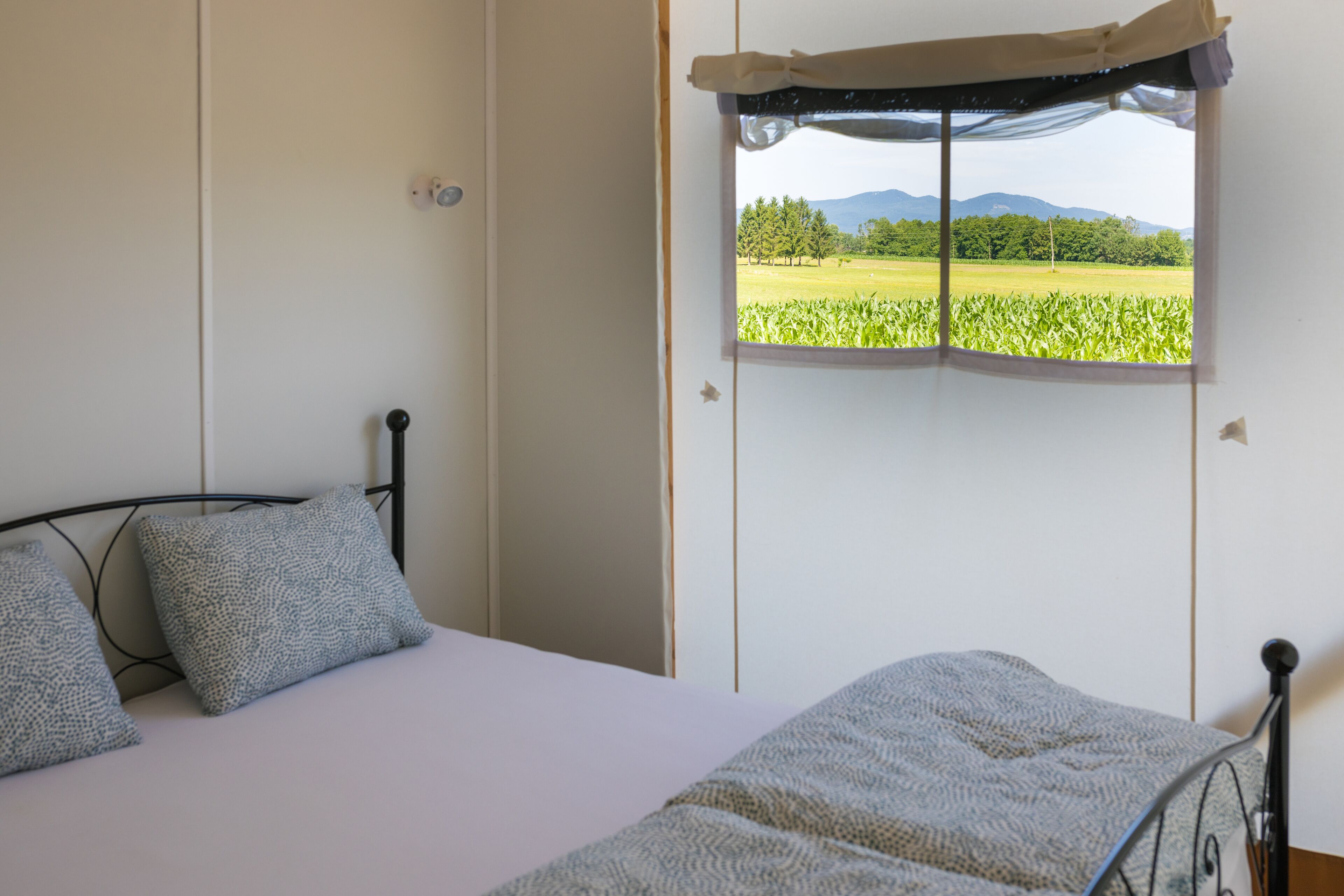 A bedroom with a bed, a window with a view of a field and mountains, and a curtain.