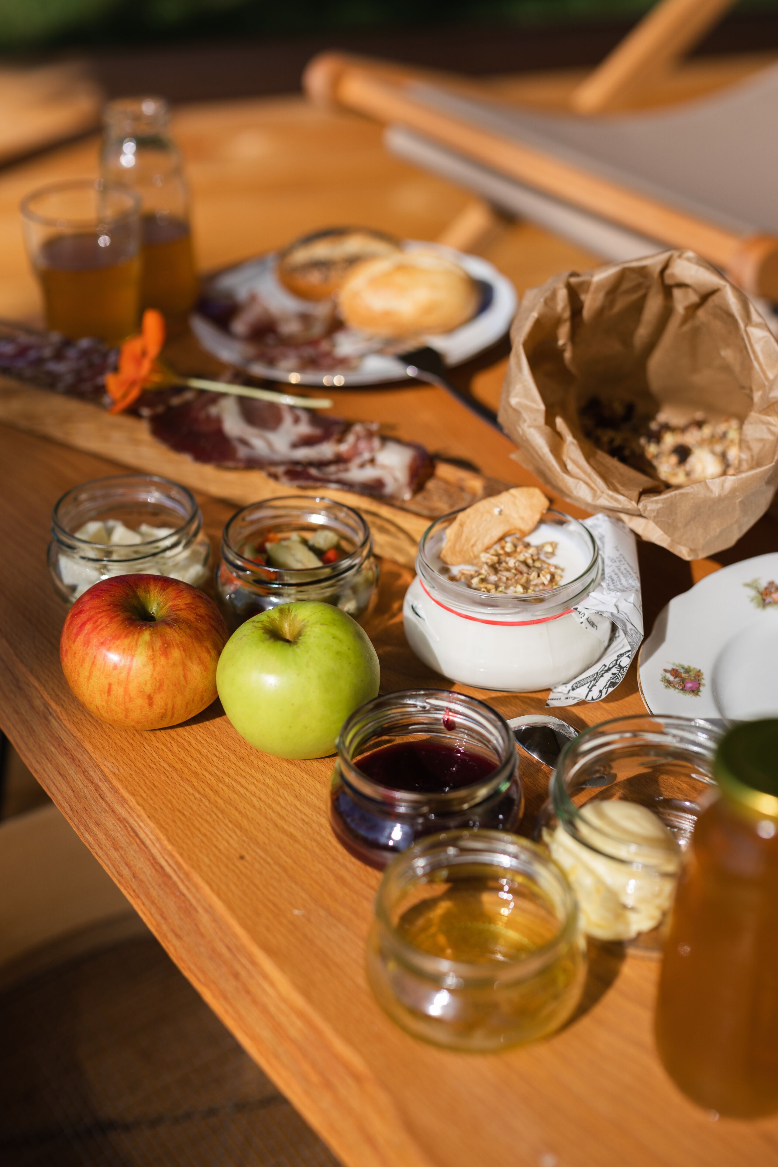 A wooden table with various food items and jars, including apples, bread, and condiments.