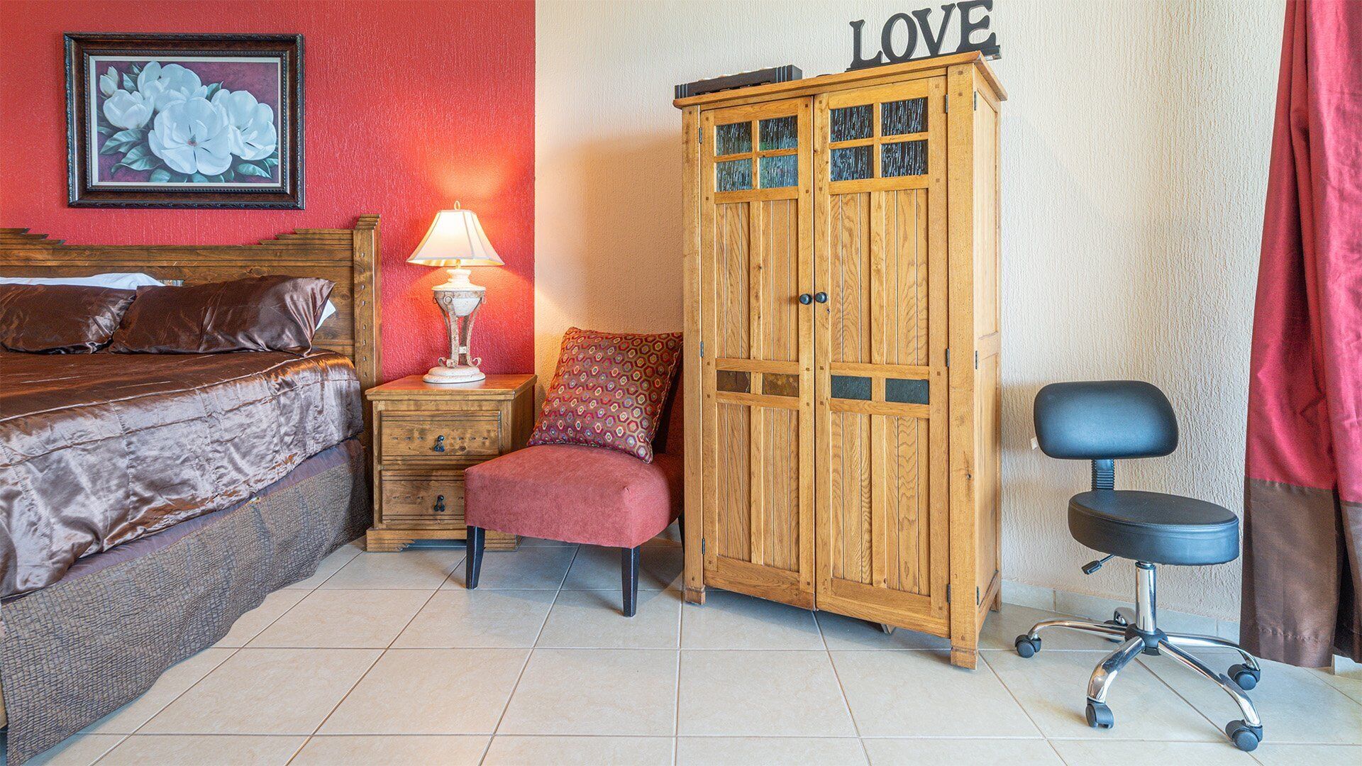 Une chambre avec un lit, une armoire en bois, un bureau avec une lampe, une chaise et un mur orné d’un panneau indiquant le mot « AMOUR ».