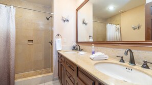 Un baño con ducha a ras de suelo, dos lavamanos, un espejo grande y decoración de mariposas en la pared.