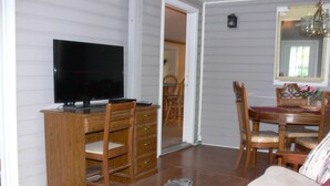 Quarto com escrivaninha de madeira, televisão, mesa de jantar com cadeiras e espelho.