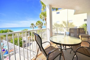 A balcony with a glass table and chairs, overlooking a beach. - West Coast Vistas  Beach front 3 bedrooms two bath 1D (Indian Rocks Beach)