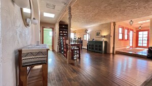 Une pièce spacieuse avec un plancher en bois, un coin repas comprenant des chaises et une table, une bibliothèque intégrée et une grande fenêtre donnant sur un beau paysage.