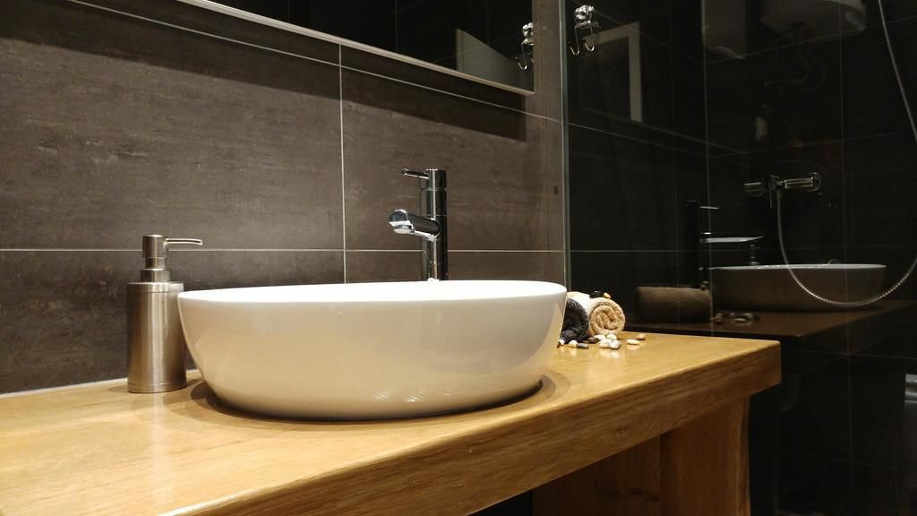 A modern bathroom with a large white sink, a handheld showerhead, and a mirror above the sink.
