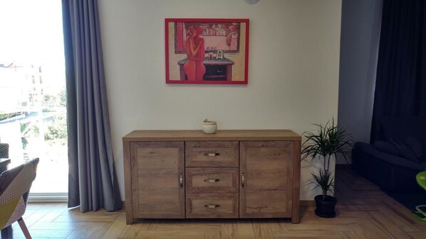 A wooden cabinet with drawers, a small plant, and a painting on the wall.