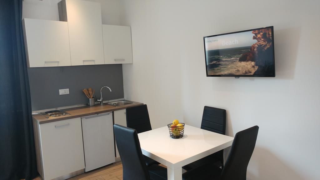 Una cocina compacta con armarios blancos, lavavajillas integrado y un comedor con una mesa y cuatro sillas. Un televisor montado en la pared muestra una escena de playa.