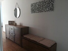 Una habitación con un banco de madera, un mueble con cajones, un espejo y un adorno geométrico en la pared.