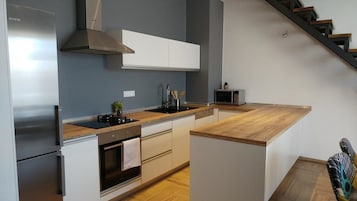 Una cocina moderna con refrigerador de acero inoxidable, horno empotrado, microondas y encimera de madera.