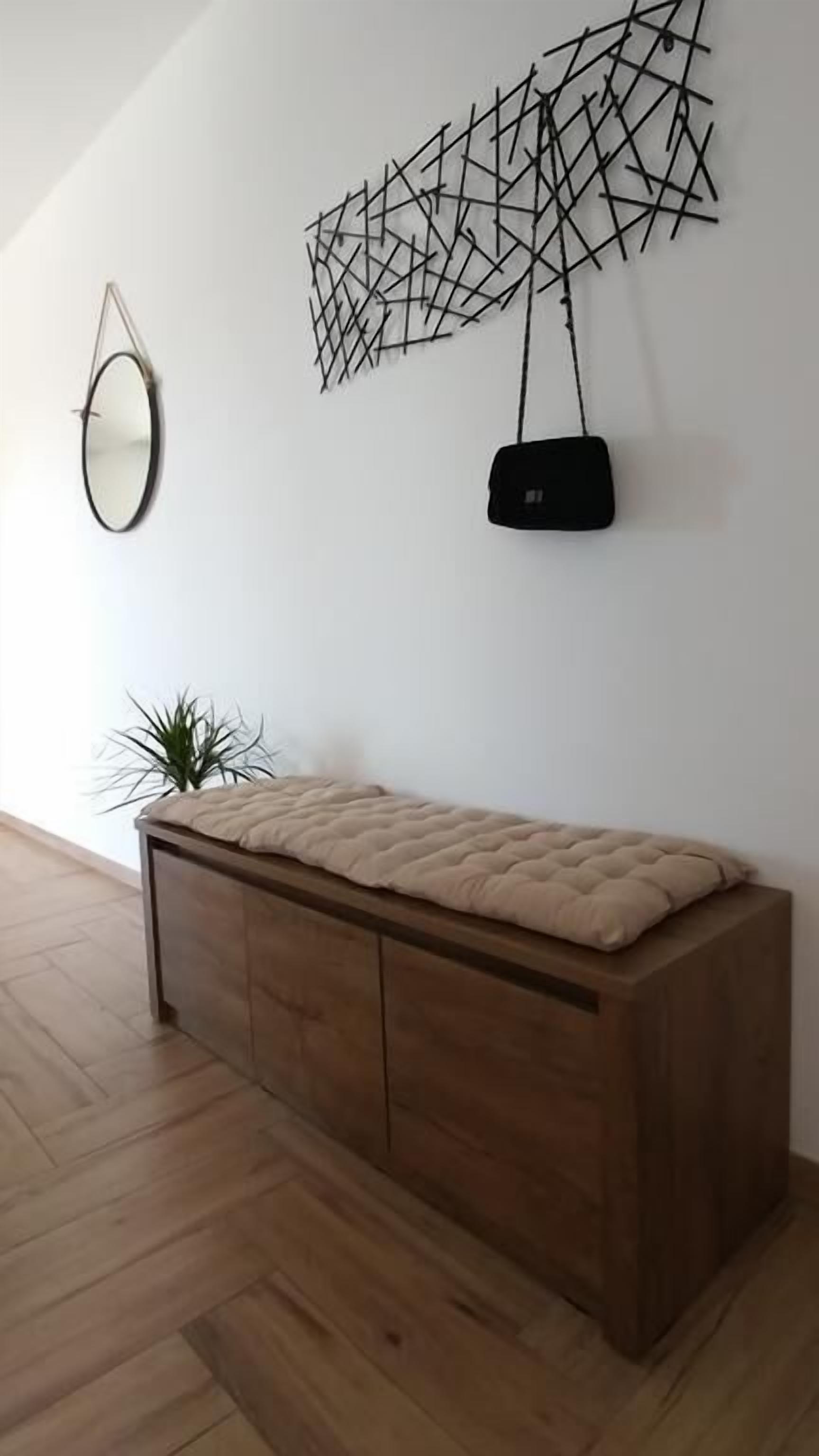 Una habitación moderna con un banco de madera, una obra de arte geométrica en la pared, un espejo redondo y un objeto negro colgado.