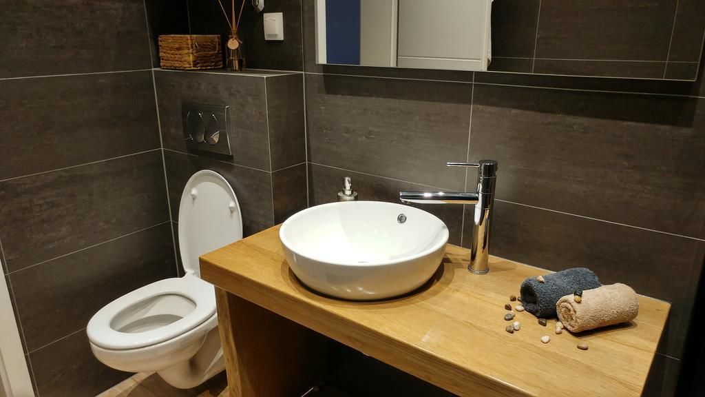 Moderni kylpyhuone, jossa on valkoinen wc-istuin, pyöreä pesuallas ja puinen allaskaappi.
