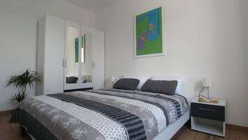 A bedroom with a bed, a wardrobe, a nightstand, and a painting on the wall.