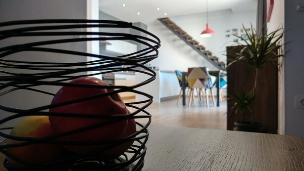 Eine moderne Küche mit einem Holztisch, einem schwarzen Metallkorb mit Äpfeln und einer Treppe, die zu einer oberen Ebene führt.