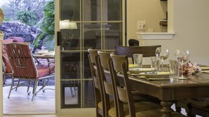 A dining area with a table set for four, chairs, and a glass partition. - Hale Alaula - Ocean View: Private Home Near Kona Town w/Spa, AC, Spacious Lanai (Kailua Kona)