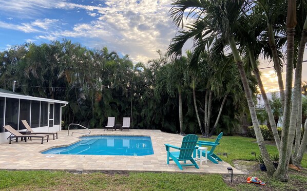 A backyard with a swimming pool, lounge chairs, and a table.