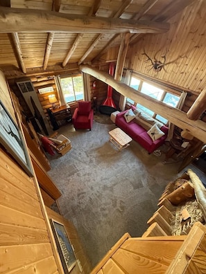 A cozy cabin interior with a wooden ceiling, a red sofa, a small table, and a fireplace.