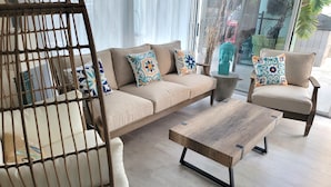 Una sala de estar moderna con un sofá, dos sillones, una mesa de centro y una silla de mimbre.