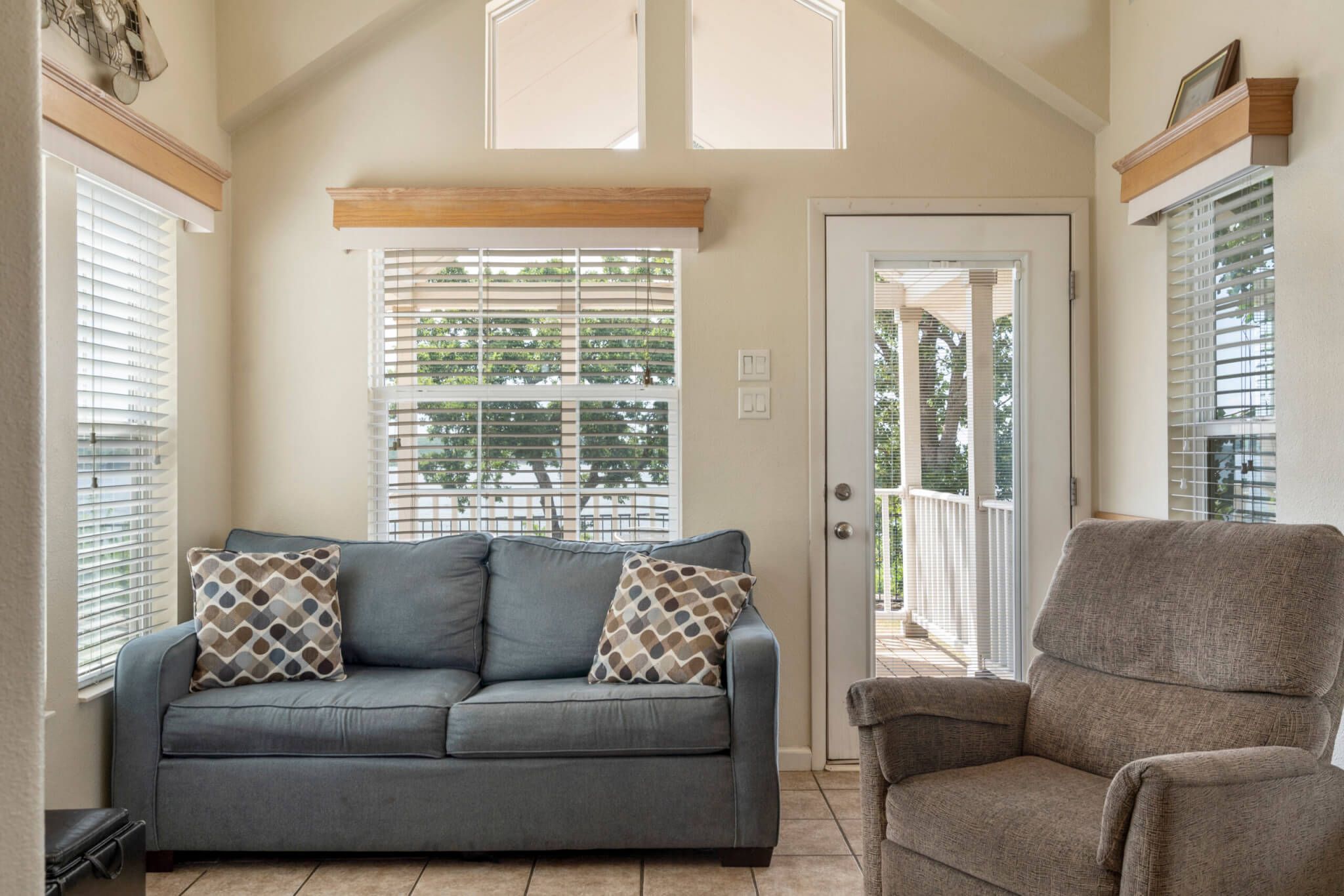 A room with a grey sofa, a brown armchair, and a door leading to an outdoor balcony.
