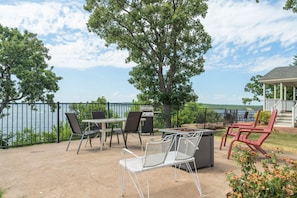 Un patio exterior con una parrilla, sillas y vistas al lago.