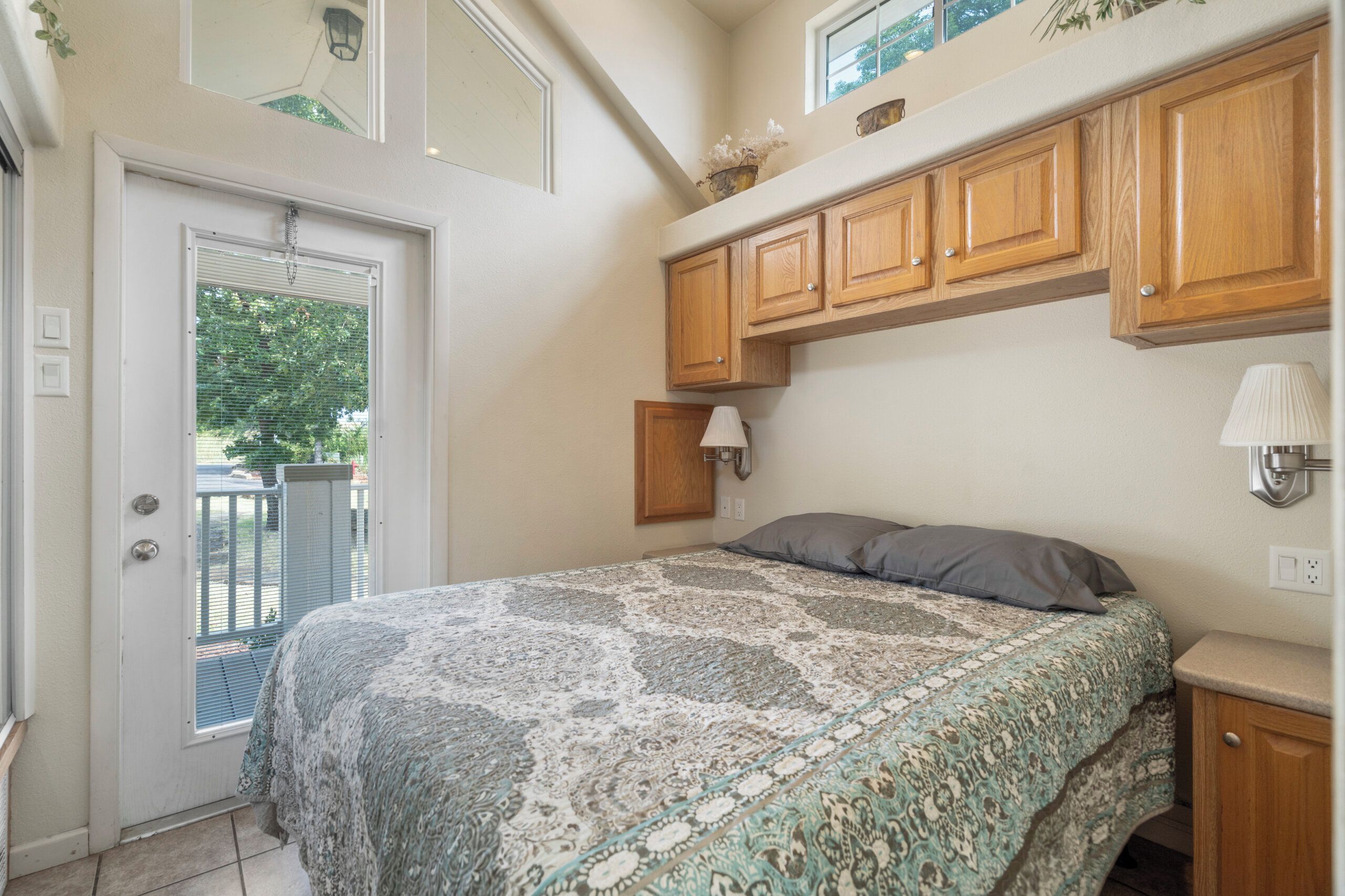 A bedroom with a bed, wooden cabinets, a window, and a door.