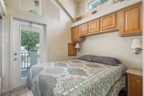 A bedroom with a bed, wooden cabinets, a window, and a door. - Cozy Retreat at CrossTimbers Marina (sperry)