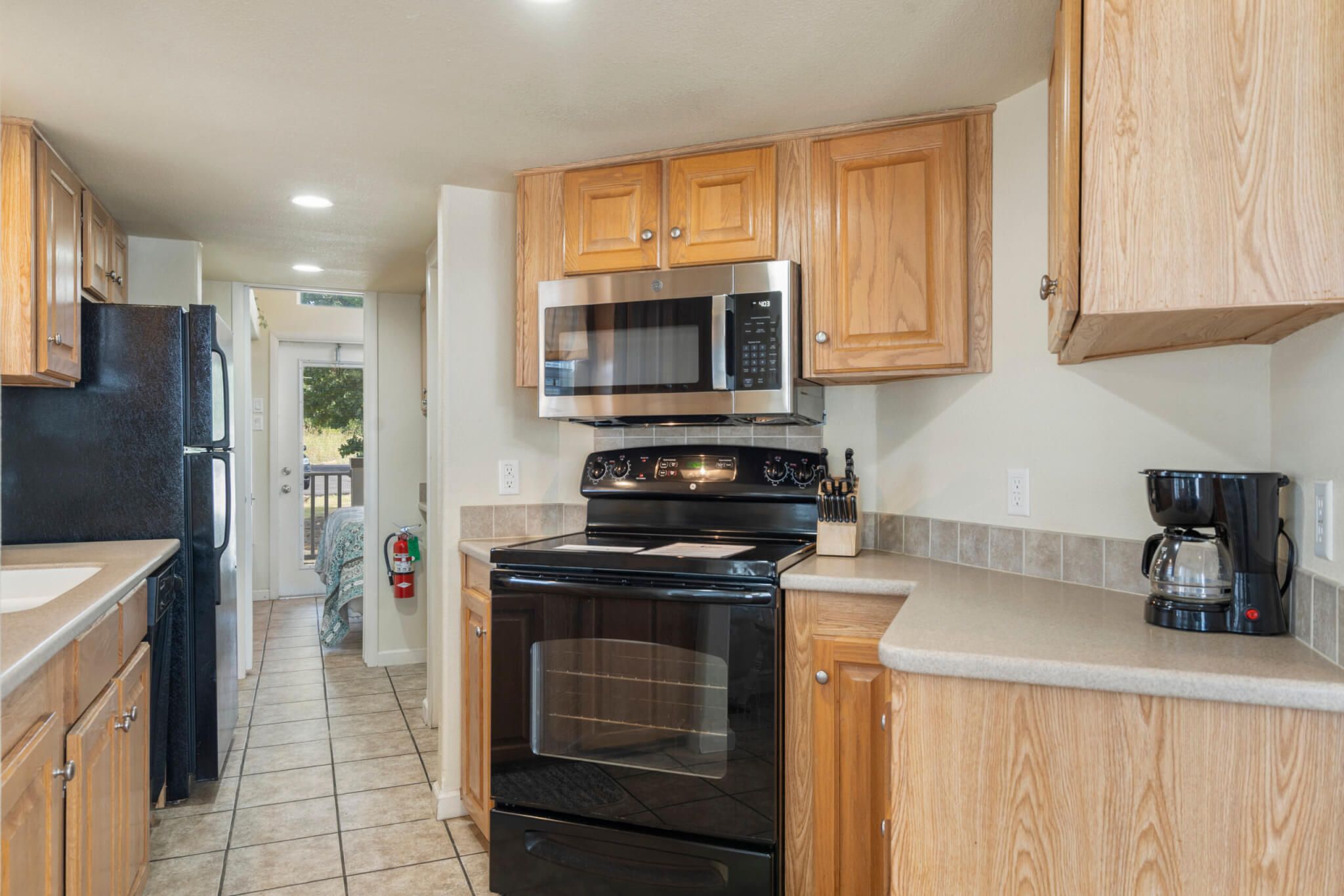 A kitchen with wooden cabinets, a stainless steel microwave, a black stove, and a coffee maker.