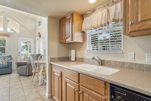 A kitchen with wooden cabinets, a sink, and a window with blinds. - Cozy Retreat at CrossTimbers Marina (sperry)