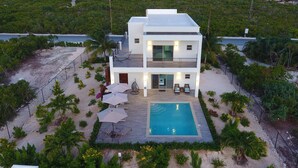 Une maison moderne à deux étages avec une piscine, entourée d’une végétation tropicale et offrant une vue sur l’océan.