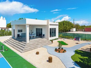 Una casa moderna con patio, piscina exterior y un pequeño jardín.