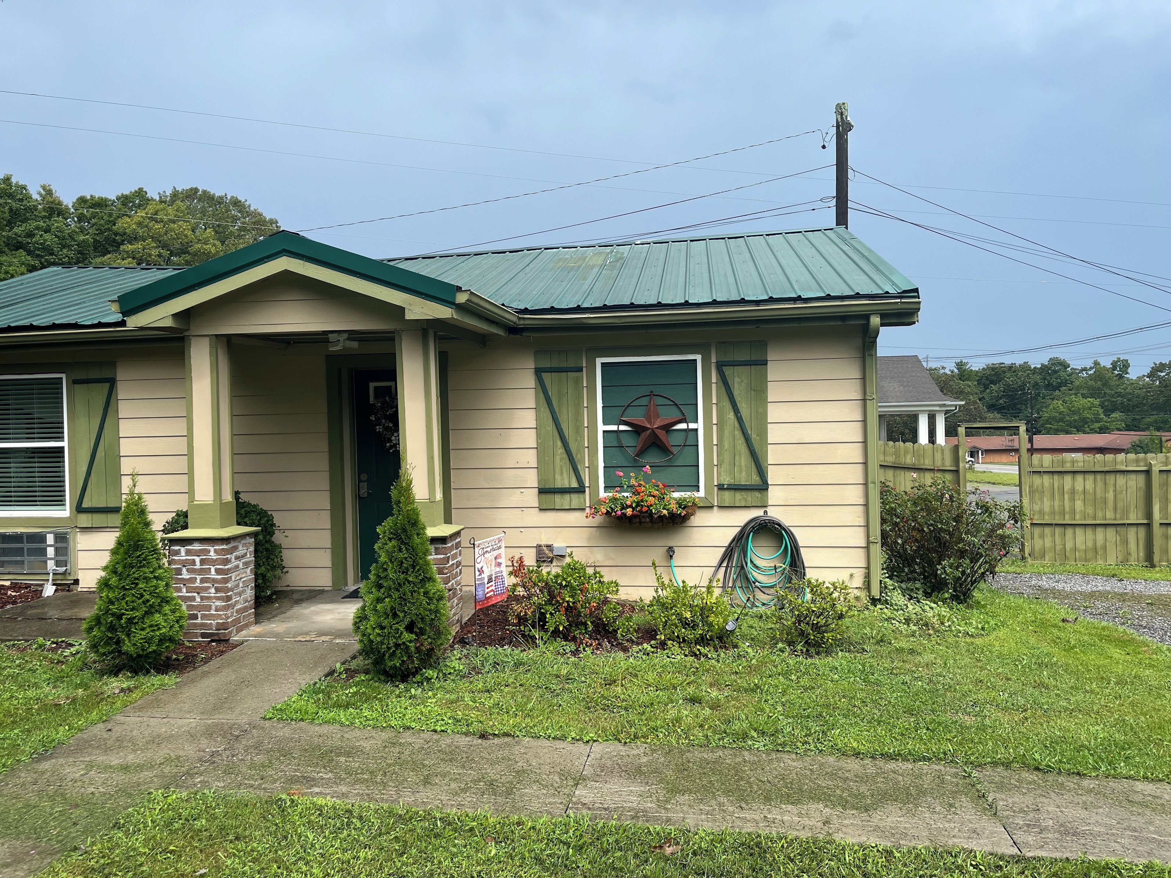 Uma casa térrea com telhado verde, alicerce de tijolos e varanda frontal.