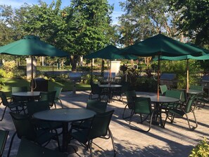 An outdoor patio area with round tables and chairs, green umbrellas, and barbecue grills. - Luxury 3 bed  Resort Style Amenities (Naples)