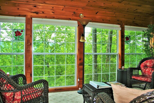A cozy room with wicker furniture, large windows, and a view of greenery.