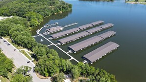 An aerial view of a marina with multiple covered docks and a parking lot adjacent to a forested area.