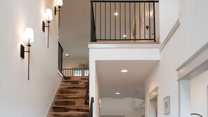 A staircase with wooden steps leading to a balcony, a blue sofa in the living area, and a patterned rug on the floor.