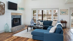 A modern living room with a fireplace, blue sofa, and large windows offering a view of the outdoors.