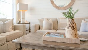 En stue med en beige sofa, et sofabord med en vase og et fad, et rundt spejl på væggen og en lampe på et sidebord.