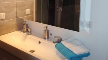 A modern bathroom with a large mirror, a white sink, and a glass shower enclosure.