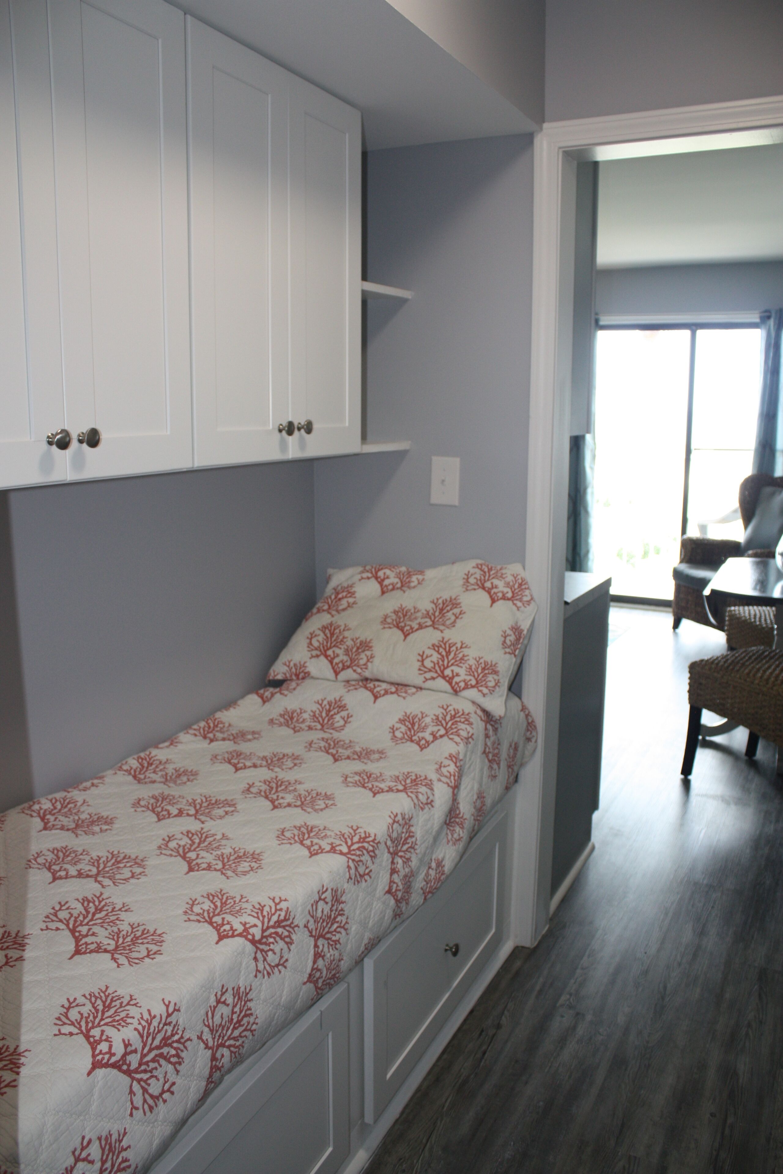 A compact bedroom with a bed, built-in white cabinets, and a view of a dining area.