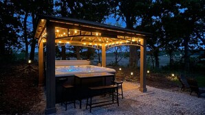 A hot tub under a covered pavilion with string lights, surrounded by trees. - 4BR Lodge Near Lake Geneva - Sitting Pool, Hot Tub, Sauna, Lake Views on 3 Acres (Lake Geneva)