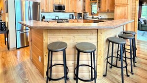 A modern kitchen with wooden cabinets, stainless steel appliances, a large island with bar stools, and a hanging light fixture. - 4BR Lodge Near Lake Geneva - Sitting Pool, Hot Tub, Sauna, Lake Views on 3 Acres (Lake Geneva)