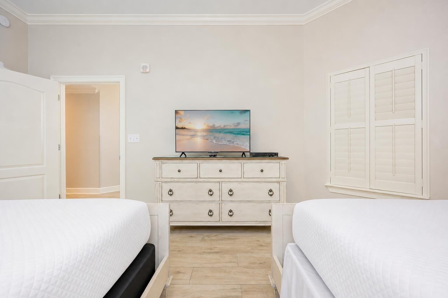 A bedroom with two beds, a dresser, and a painting of a beach scene.