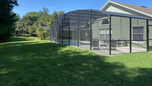 A covered outdoor area with a pool, seating, and a house in the background. - GORGEOUS POOL HOME IN QUIET TRANQUIL SETTING CLOSE TO ATTRACTIONS & OUTLETS (Kissimmee)