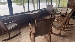 Ett rum med utsikt över en sjö, inrett med gungstolar och ett bord, allt i trä.