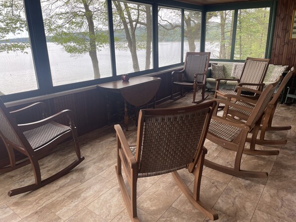 A room with a view of a lake, furnished with wooden rocking chairs and a table.