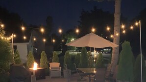 An outdoor patio area with a table and chairs, surrounded by string lights and a large umbrella. - ★★★★★Charlevoix 5 Star-rated Cottage★★★★★ (Charlevoix)
