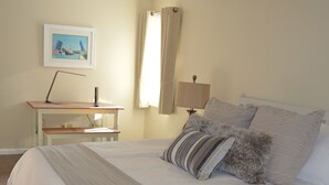A neatly made bed with a white comforter and several pillows, a desk with a lamp, and a ceiling fan in a room with beige walls. - ★★★★★Charlevoix 5 Star-rated Cottage★★★★★ (Charlevoix)