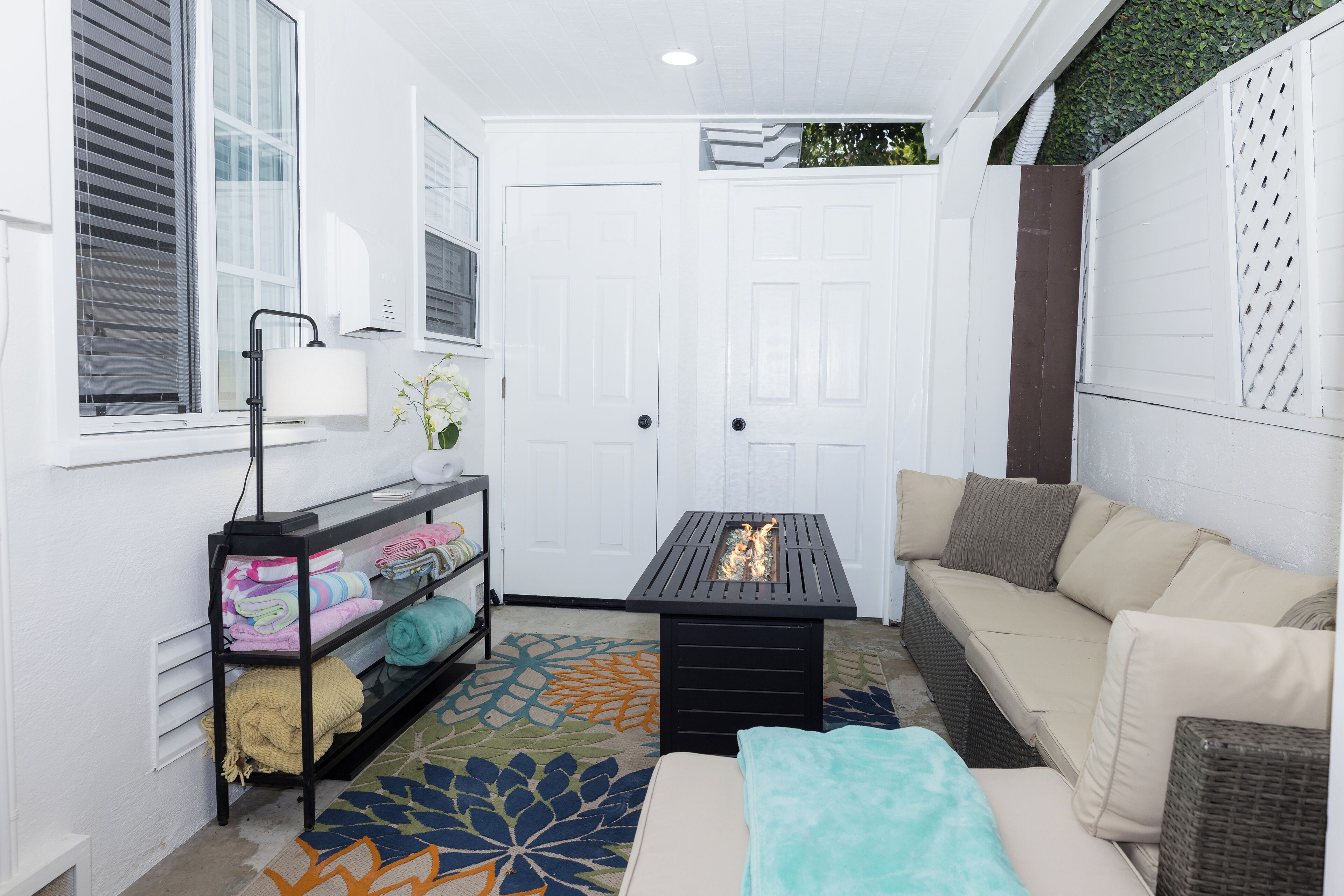 A cozy room with a sofa, a small table, a shelf with folded blankets, and a patterned rug.